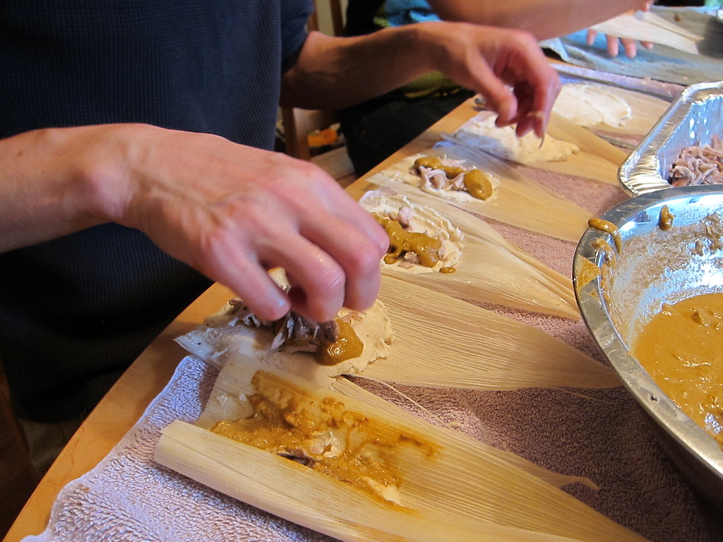 Hands filling and folding tamales fresh, ready to steam