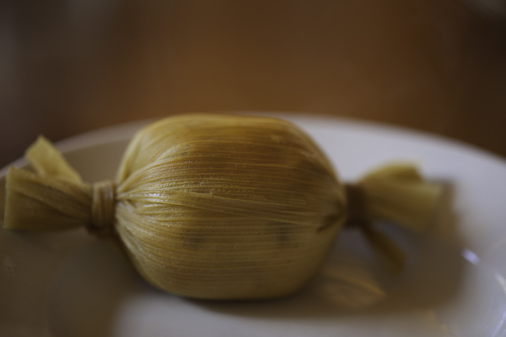 A tamal wrapped in a corn husk, tied at both ends